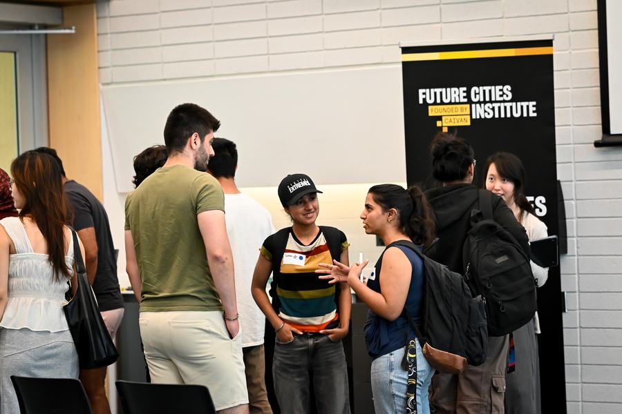A faculty member speaking with students in front of a Future Cities Institute banner